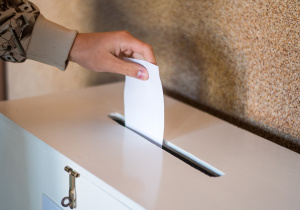 ręka z kartą do głosowania wrzucaną do urny