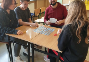 uczniowie i nauczyciel grają w grę planszową