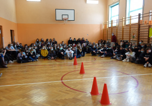 grupa uczniów siedzi na podłodze w sali gimnastycznej